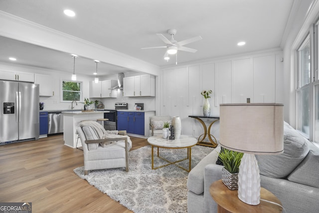 living room with ceiling fan, sink, light wood-type flooring, and crown molding