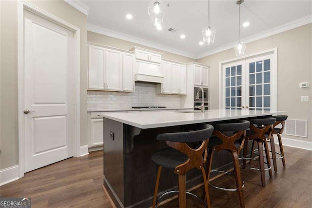 kitchen with white cabinetry, sink, hanging light fixtures, a center island with sink, and ornamental molding