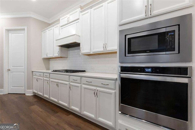 kitchen featuring dark hardwood / wood-style floors, backsplash, crown molding, white cabinets, and appliances with stainless steel finishes