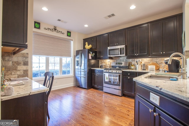 kitchen featuring light stone counters, stainless steel appliances, visible vents, dark brown cabinetry, and a sink