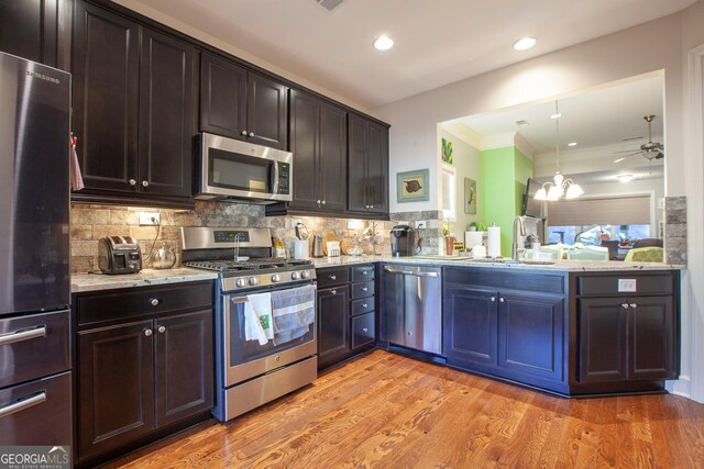 kitchen with light stone countertops, light wood-type flooring, backsplash, stainless steel appliances, and sink