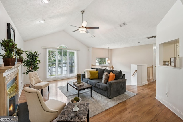 living room with a textured ceiling, ceiling fan, light hardwood / wood-style floors, and vaulted ceiling