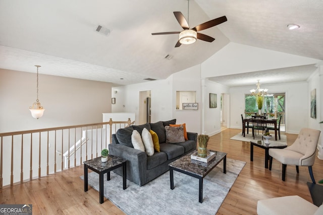 living room featuring ceiling fan with notable chandelier, vaulted ceiling, a textured ceiling, and light hardwood / wood-style flooring