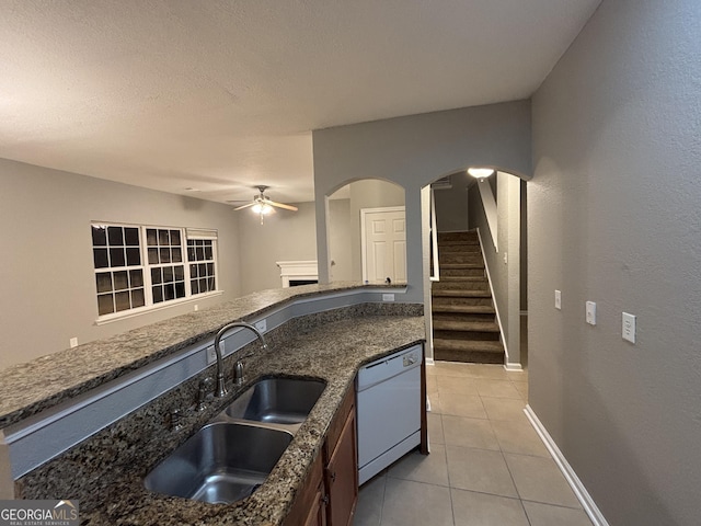 kitchen featuring dishwasher, light tile patterned floors, dark stone counters, ceiling fan, and sink