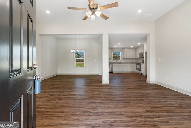 unfurnished living room featuring recessed lighting, dark wood finished floors, baseboards, and ceiling fan with notable chandelier