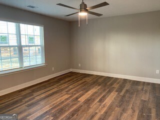 spare room featuring ceiling fan, visible vents, baseboards, and dark wood-style flooring