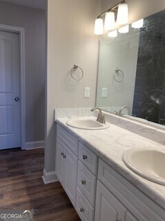 full bath featuring double vanity, baseboards, a sink, and wood finished floors