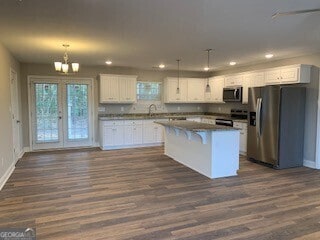 kitchen featuring dark wood-style flooring, decorative light fixtures, stainless steel appliances, white cabinetry, and a kitchen island