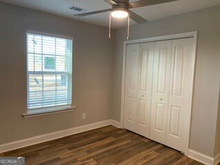 unfurnished bedroom with dark wood-style flooring, a closet, visible vents, ceiling fan, and baseboards