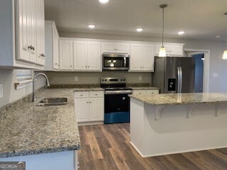 kitchen with stainless steel appliances, a sink, white cabinets, hanging light fixtures, and dark wood finished floors