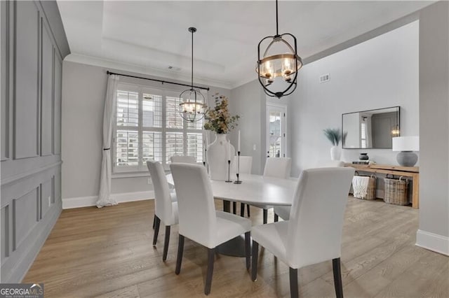 dining area featuring crown molding, a notable chandelier, light hardwood / wood-style floors, and a tray ceiling