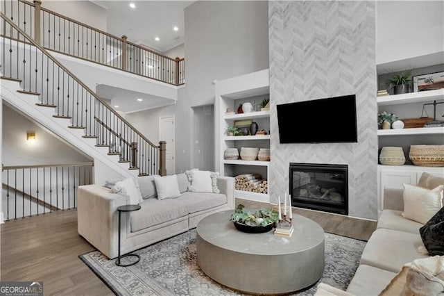 living room with a tiled fireplace, hardwood / wood-style floors, a towering ceiling, and built in features