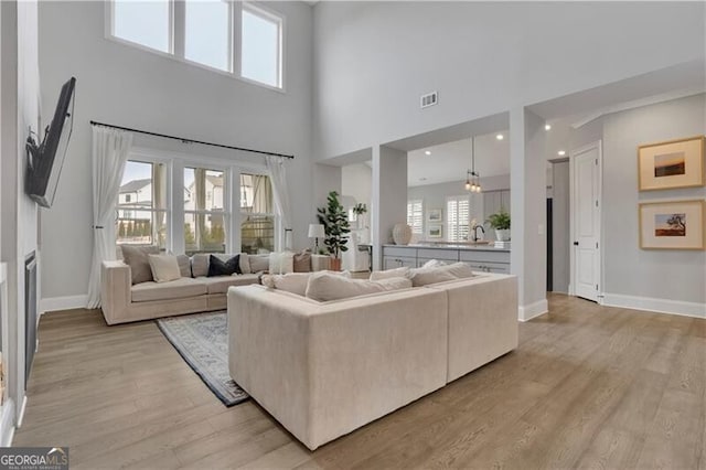 living room with a high ceiling, a healthy amount of sunlight, and light hardwood / wood-style flooring