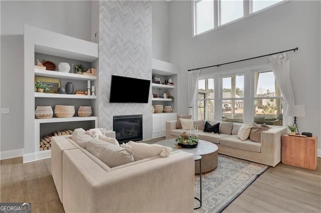 living room featuring built in shelves, a large fireplace, a high ceiling, and light wood-type flooring