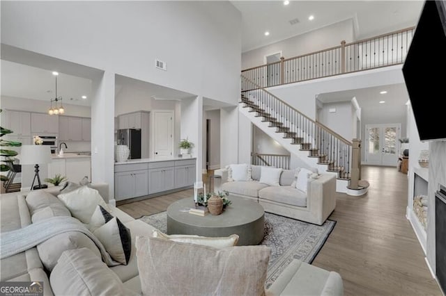 living room featuring an inviting chandelier, sink, light hardwood / wood-style floors, and a high ceiling