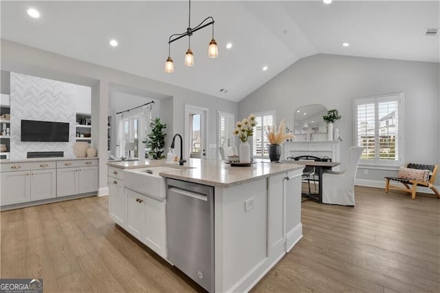 kitchen featuring hanging light fixtures, dishwasher, light stone countertops, and an island with sink