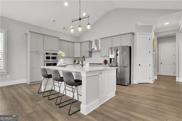 kitchen featuring wall chimney range hood, light hardwood / wood-style flooring, a breakfast bar, stainless steel appliances, and a center island with sink