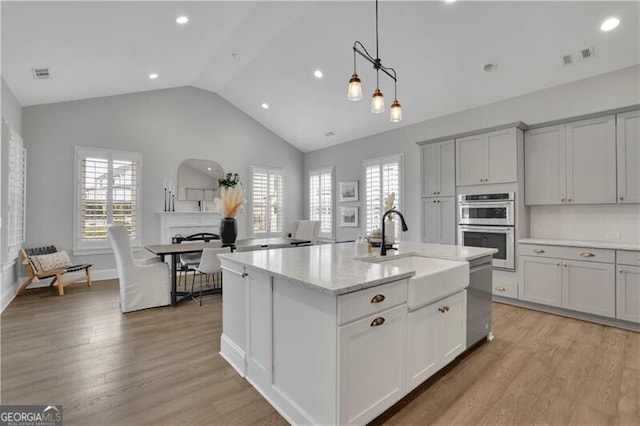 kitchen featuring sink, light stone counters, an island with sink, stainless steel appliances, and backsplash