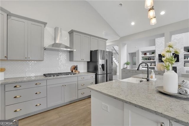 kitchen with lofted ceiling, wall chimney range hood, gray cabinets, stainless steel appliances, and light stone countertops