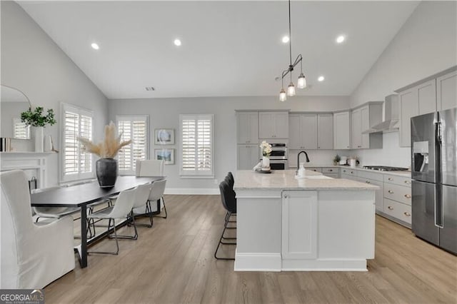 kitchen featuring appliances with stainless steel finishes, pendant lighting, an island with sink, sink, and light stone countertops