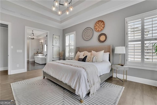 bedroom featuring hardwood / wood-style flooring, crown molding, an inviting chandelier, and ensuite bath