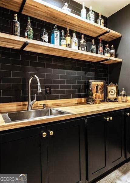 bar featuring light wood-type flooring, sink, decorative backsplash, and butcher block countertops