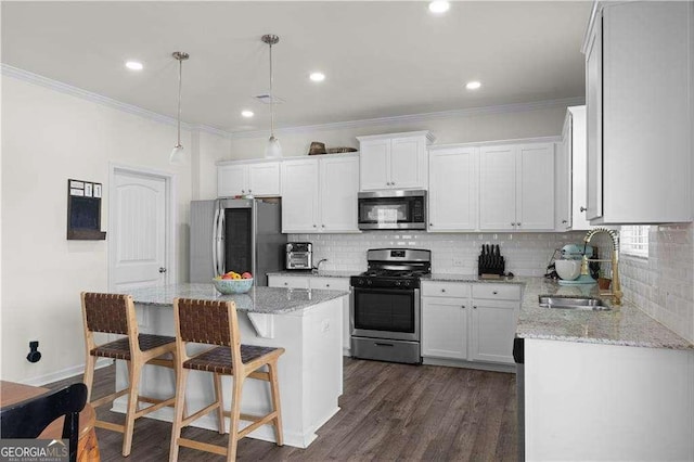 kitchen with sink, stainless steel appliances, a kitchen island, tasteful backsplash, and white cabinets