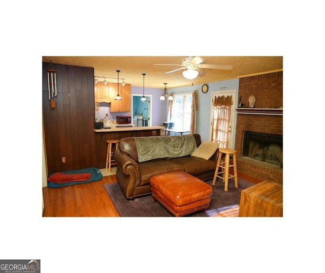 living room featuring ceiling fan, hardwood / wood-style floors, and a brick fireplace