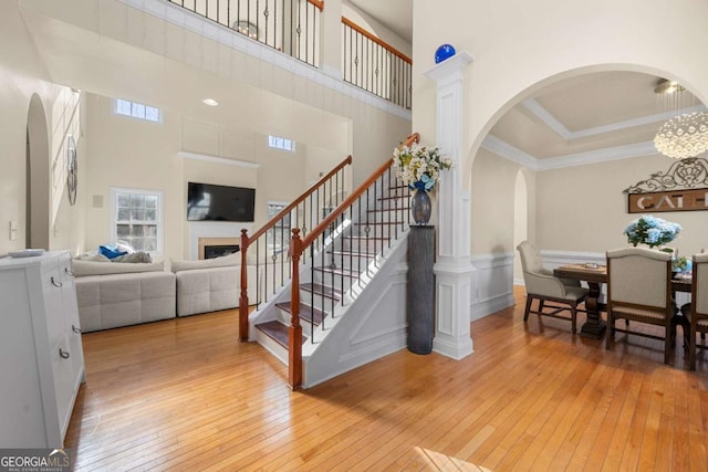 stairs with a towering ceiling, hardwood / wood-style flooring, ornamental molding, and a notable chandelier