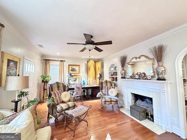 living room featuring wood-type flooring, ornamental molding, built in features, and ceiling fan