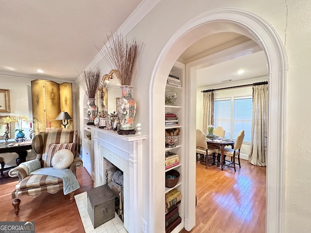 corridor with ornamental molding, built in shelves, and light hardwood / wood-style flooring