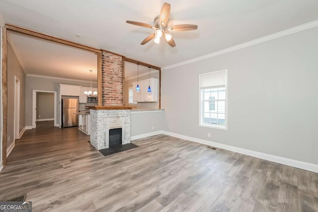 unfurnished living room featuring hardwood / wood-style flooring, ornamental molding, ceiling fan with notable chandelier, and a brick fireplace