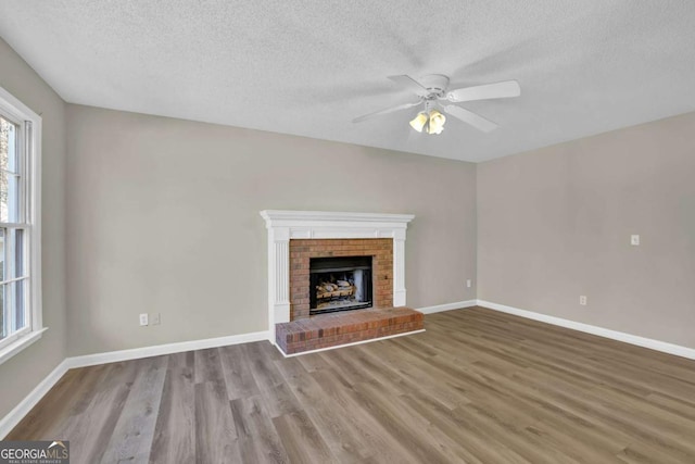 unfurnished living room with a fireplace, a textured ceiling, light hardwood / wood-style flooring, and ceiling fan