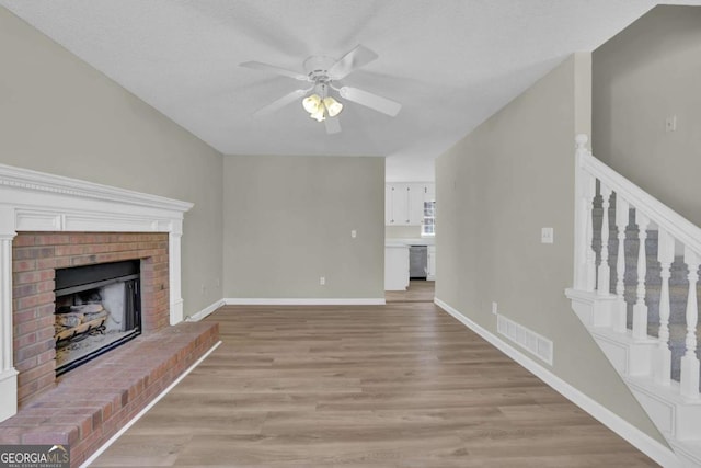 unfurnished living room featuring ceiling fan, light hardwood / wood-style flooring, a textured ceiling, and a brick fireplace