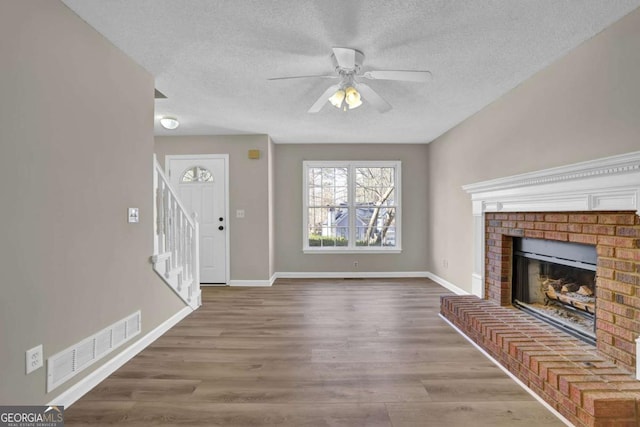 unfurnished living room with ceiling fan, a fireplace, wood-type flooring, and a textured ceiling