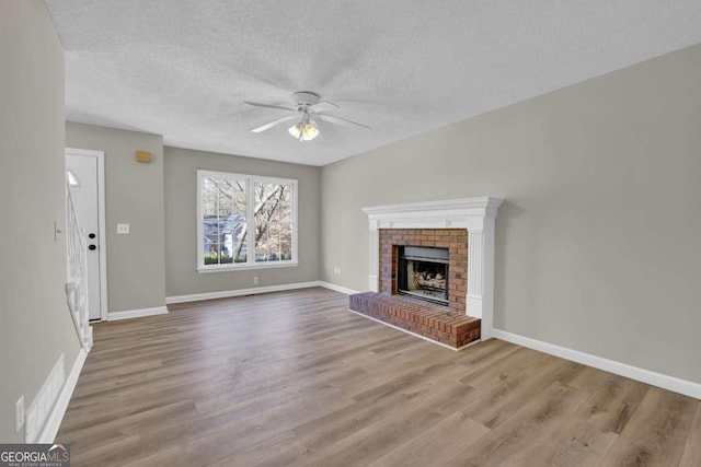 unfurnished living room featuring ceiling fan, light hardwood / wood-style floors, a textured ceiling, and a brick fireplace