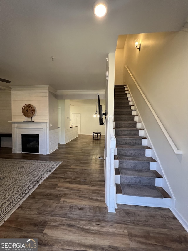 stairway featuring ornamental molding, a ceiling fan, wood finished floors, a fireplace, and baseboards