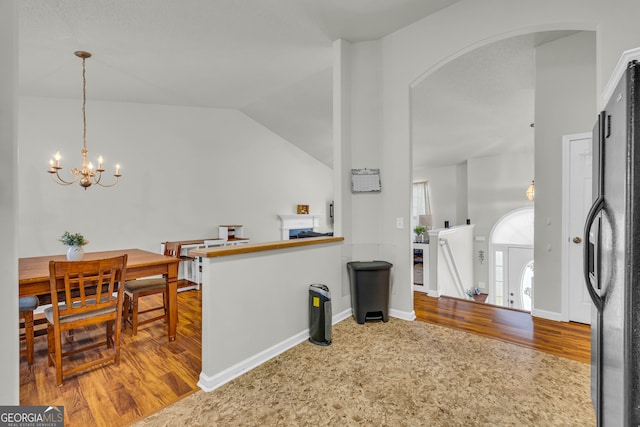 kitchen featuring a chandelier, vaulted ceiling, stainless steel refrigerator, and hanging light fixtures