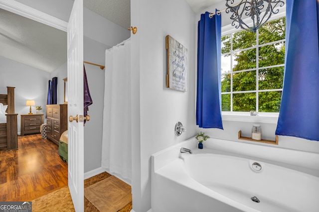 bathroom featuring plenty of natural light, lofted ceiling, a textured ceiling, and a tub