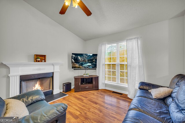 living room with hardwood / wood-style floors, ceiling fan, lofted ceiling, and a textured ceiling