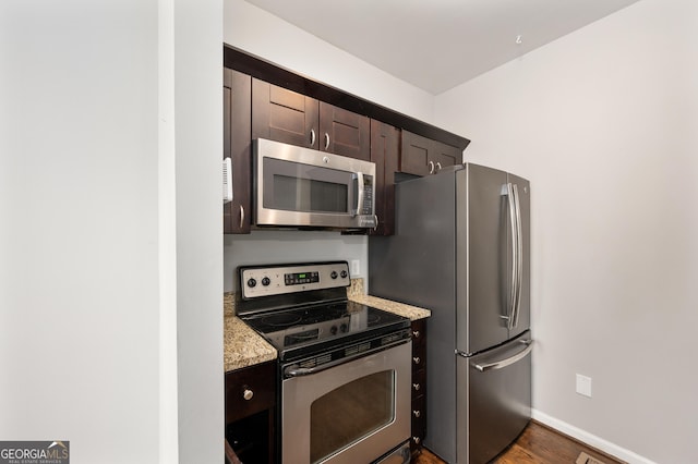 kitchen featuring stainless steel appliances, dark hardwood / wood-style floors, light stone countertops, and dark brown cabinets