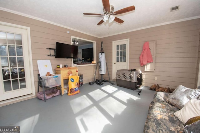 living room featuring concrete floors, ceiling fan, crown molding, and wood walls