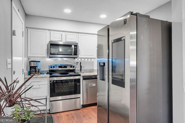 kitchen with white cabinetry, stainless steel appliances, light stone counters, and hardwood / wood-style flooring