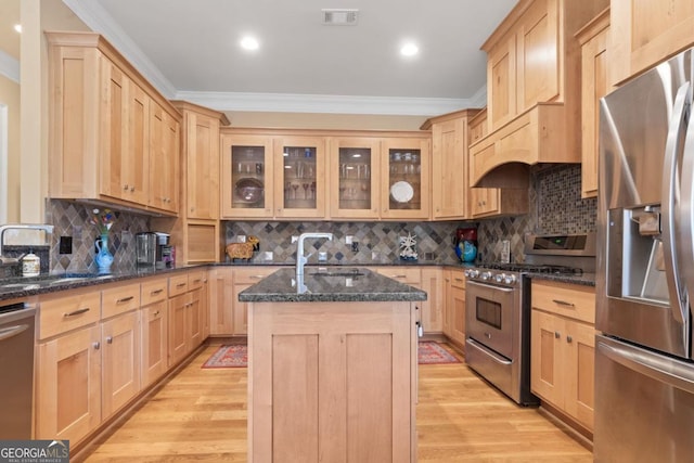 kitchen featuring decorative backsplash, dark stone counters, stainless steel appliances, sink, and a center island with sink