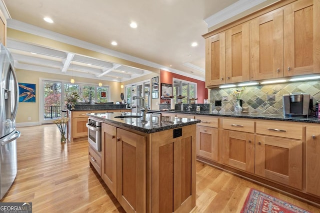 kitchen with dark stone counters, a center island with sink, sink, beamed ceiling, and stainless steel appliances