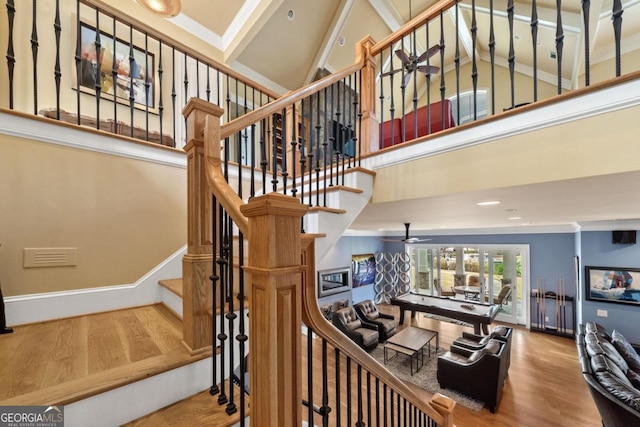 stairs featuring hardwood / wood-style floors, a towering ceiling, ceiling fan, and crown molding