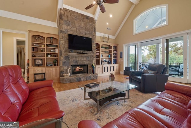 living room with ceiling fan, a stone fireplace, built in features, high vaulted ceiling, and light wood-type flooring