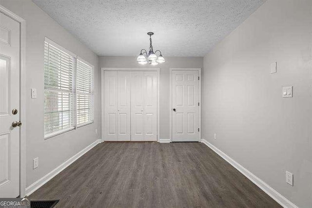 unfurnished dining area featuring a textured ceiling, an inviting chandelier, and dark wood-type flooring