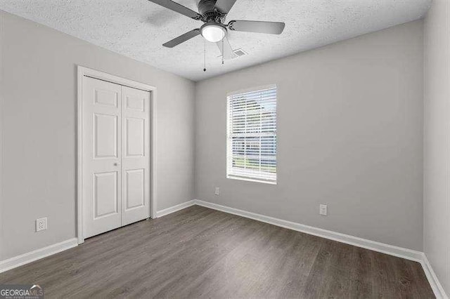 unfurnished bedroom with ceiling fan, a closet, dark hardwood / wood-style floors, and a textured ceiling