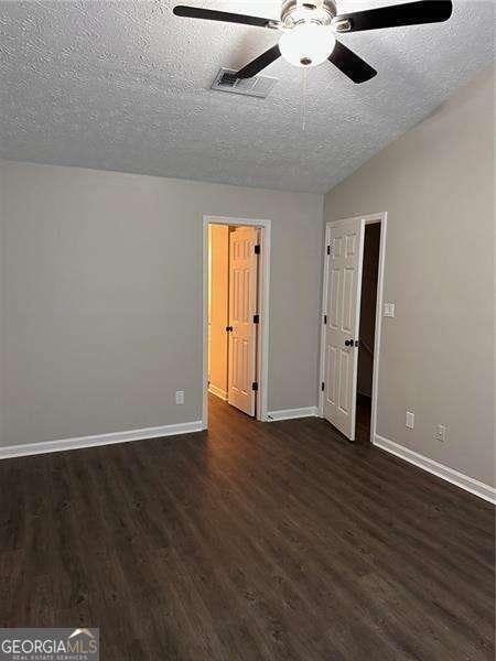 empty room featuring dark hardwood / wood-style floors, ceiling fan, lofted ceiling, and a textured ceiling